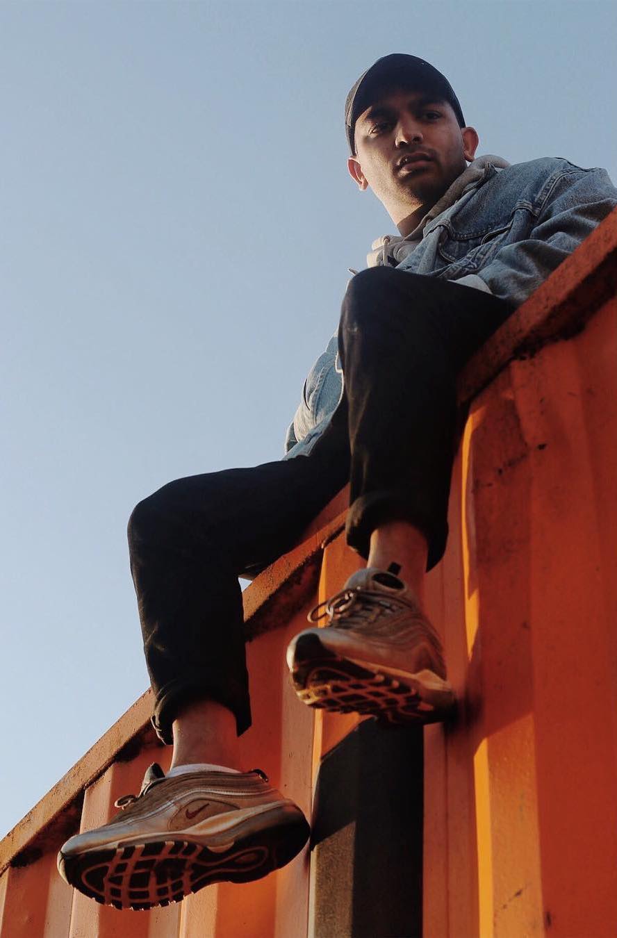 Man in denim jacket sitting on an orange shipping container