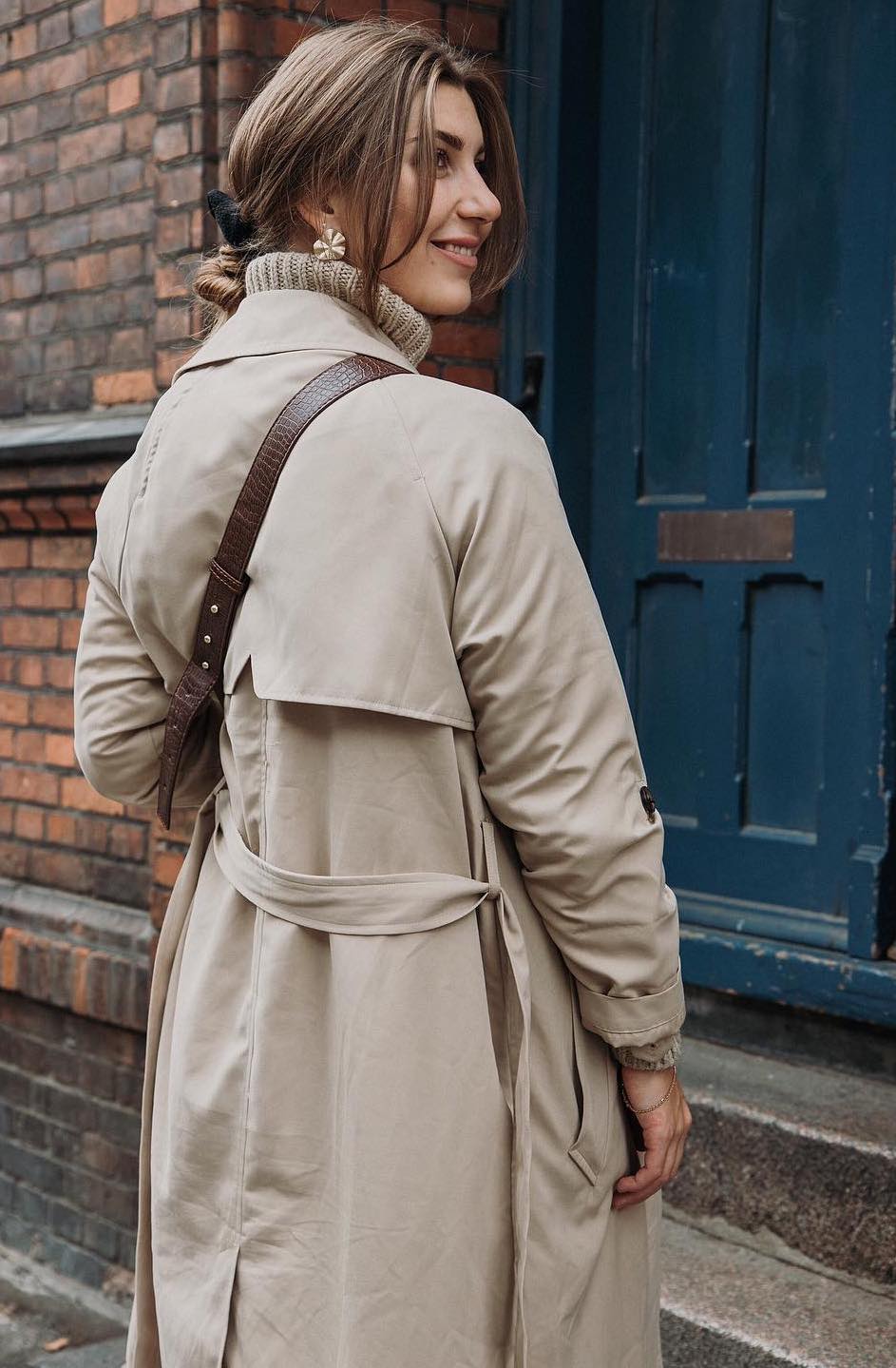 Woman in a beige trench coat looking over her shoulder